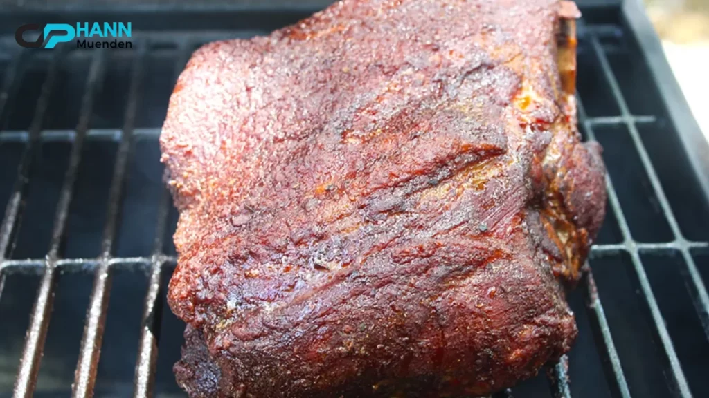 A close-up of a smoked pork butt on a grill, showing a deep, smoky crust. How long to smoke a pork butt for perfectly crisp bark?